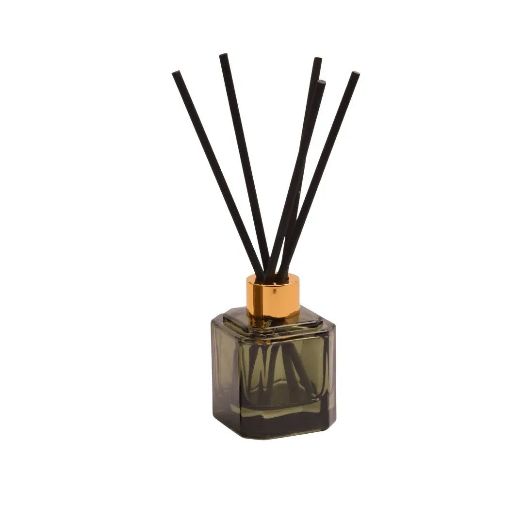 The Botanica Glass Diffuser - Wild Neroli features a square glass bottle with a gold cap and black reeds. This elegant, modern diffuser brings the fresh scent of wild neroli to any space, making it a stylish decor piece. Shown isolated on white background.