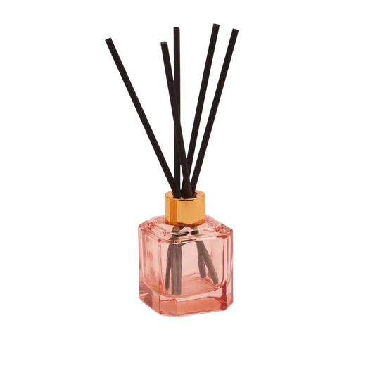 The Botanica Glass Diffuser - Saffron Rose, in pink glass with a gold cap and black reeds, brings modern elegance and a luxurious scent to any space. Perfect for enhancing your room’s style against a crisp white backdrop.