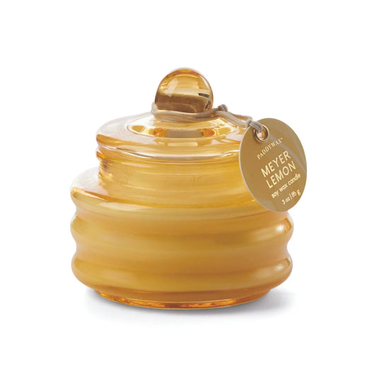 The Beam 3oz Glass Candle in Meyer Lemon features a round amber glass jar with lid and gold tag, filling any space with a captivating citrus scent and warm ambient light.