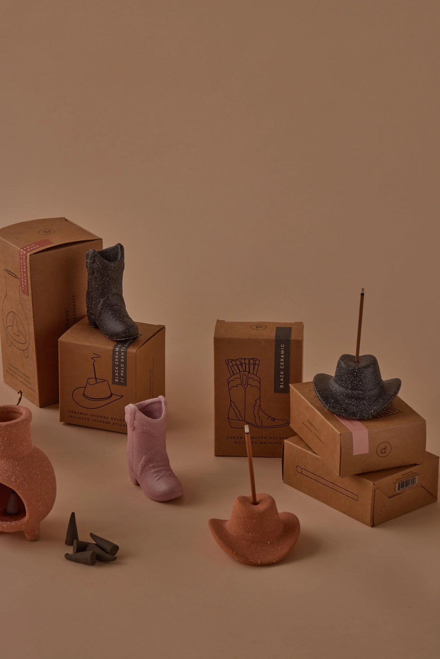 The Cowboy Hat Incense Holder - Terracotta is displayed on and around cardboard boxes against a beige background—adding a touch of vintage, western-inspired charm to your space.