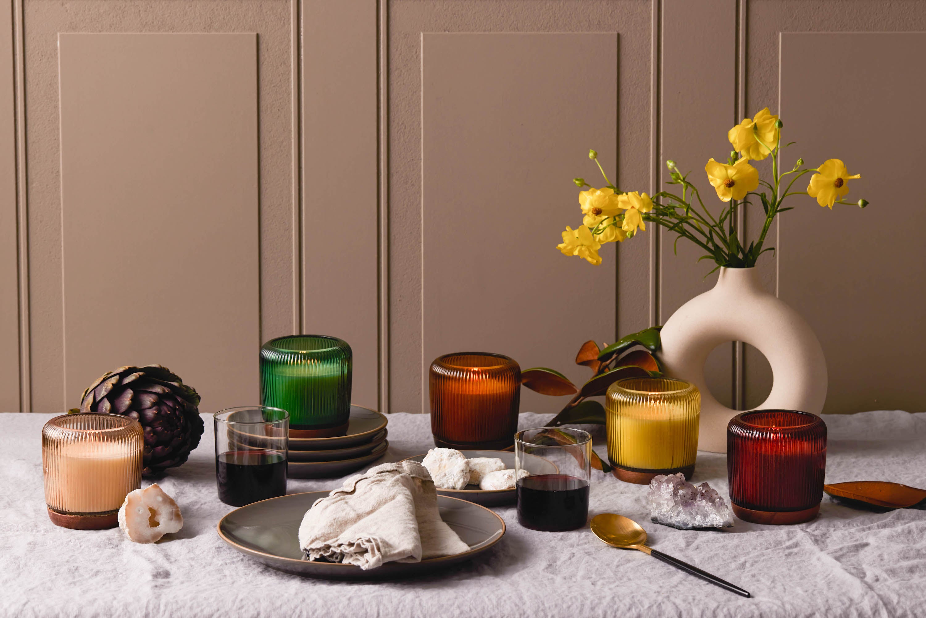 Gem Candle collection on a table with a tablecloth and a vase with a whole in the middle