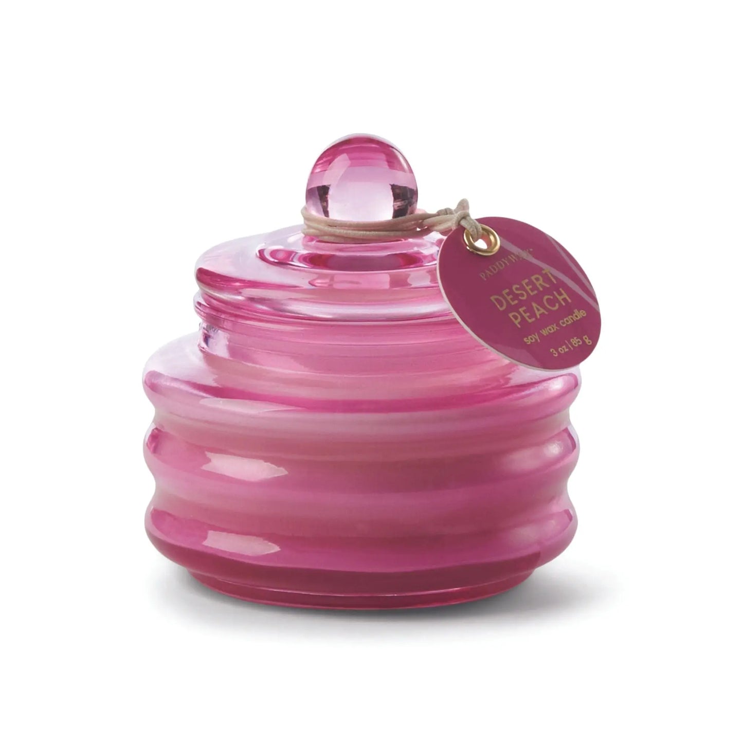 The Beam 3oz Glass Candle - Desert Peach features a pink ribbed glass jar with a round lid and label. Its gradient colors and soothing Desert Peach fragrance create a warm, inviting atmosphere in any space.