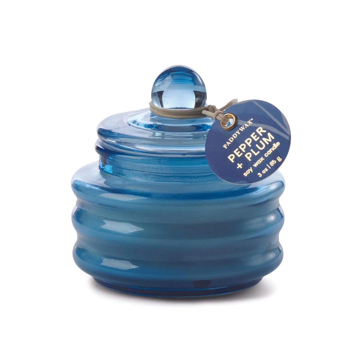 A blue Beam 3oz glass candle with round lid and Pepper + Plum tag, ideal for adding ambient light and a luxurious scent to your space.