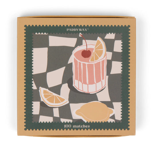 The Jumbo Boxed Matches - Cocktail features a striped cocktail glass with cherry and lemon, a lemon wedge, and a whole lemon on a checkered background. Contains 100 jumbo matches—perfect for lighting your favorite candle.