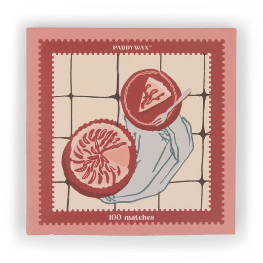 A pink Jumbo Boxed Matches - Picnic & Pie features a hand holding a plate with grapefruit slices—perfect for lighting your favorite Paddywax candle.