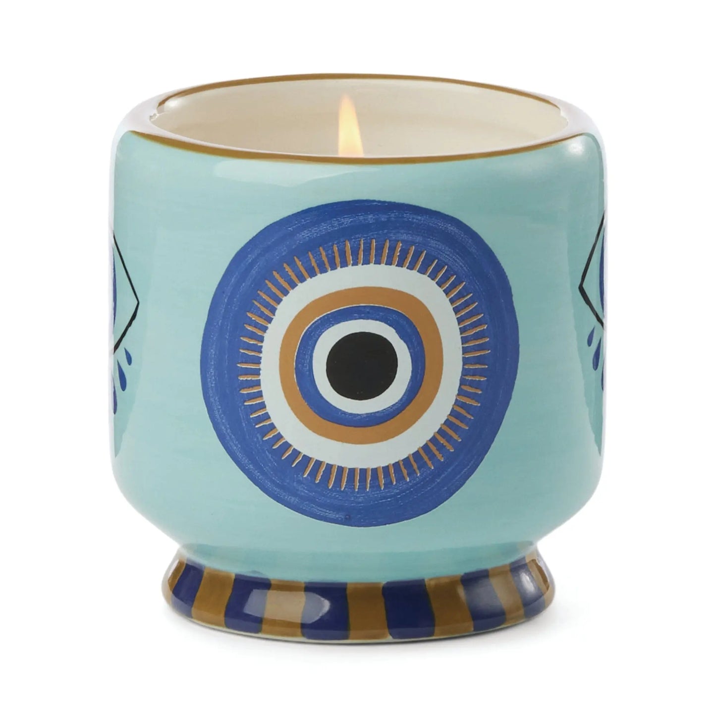 A Dopo Eye Candle - Incense & Smoke: a lit ceramic candle in a holder with hand-painted blue and gold eye accents and a striped base, shown on a white background.