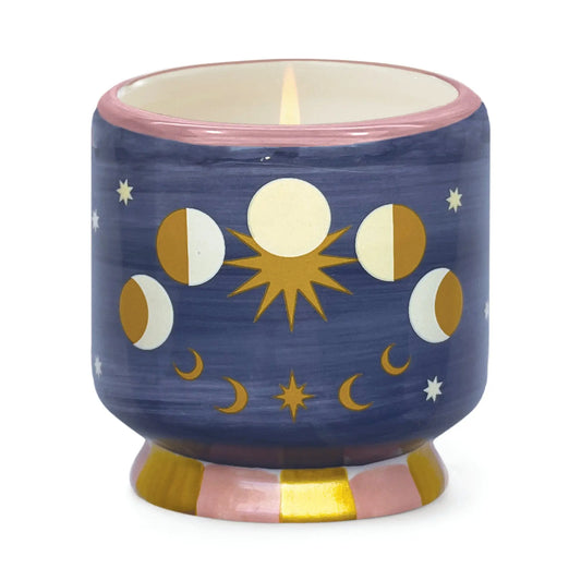 The A Dopo Moon Phases Candle—Jasmine & Rose features gold and white moon phases, stars, and a sun on blue ceramic, evoking Mediterranean travels while filling your space with bold jasmine and rose fragrance.