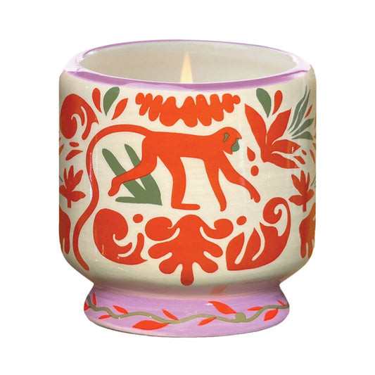 The A Dopo Jungle Candle - Coconut & Amber comes in a decorative ceramic holder with hand-painted folk art designs in red, green, and orange, featuring a charming monkey motif.
