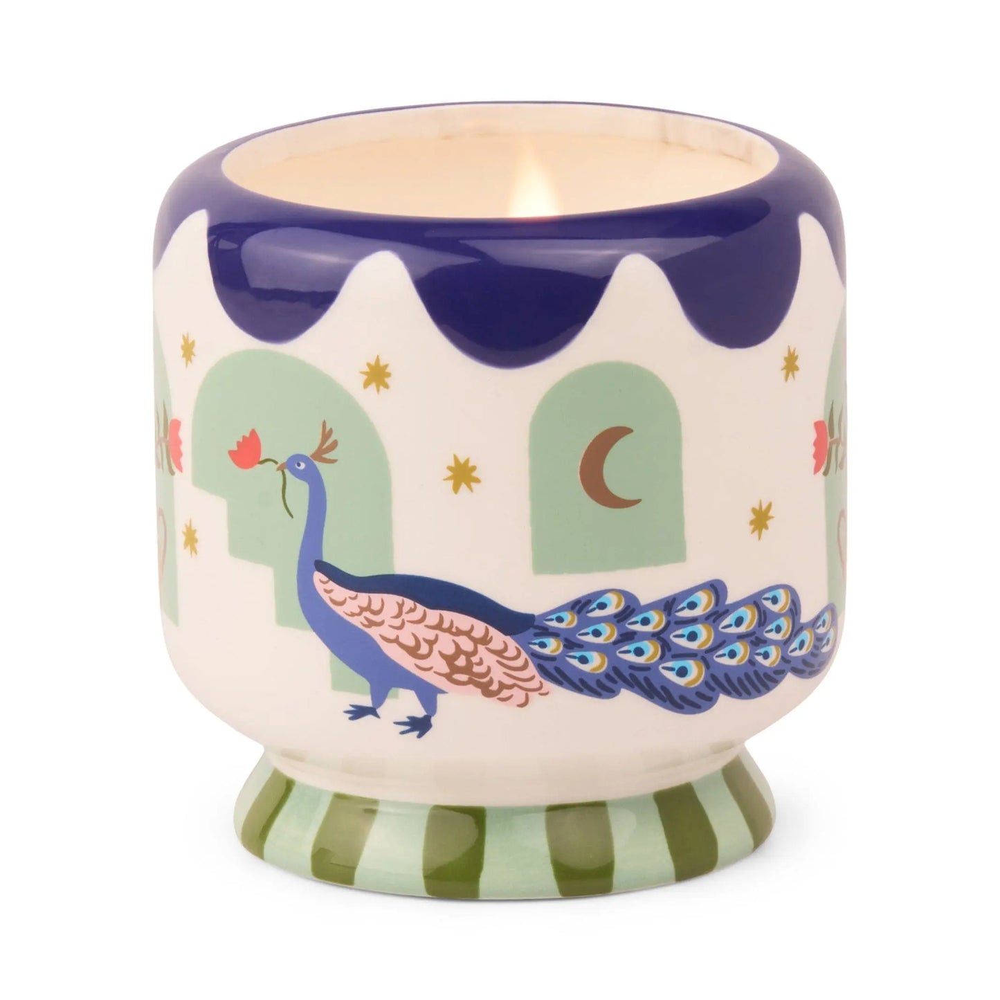 The A Dopo 8 oz Handpainted Peacock Ceramic - Misted Lime candle features a blue peacock with green arches, yellow stars, and a crescent moon in a decorative holder with a blue rim and green striped base.