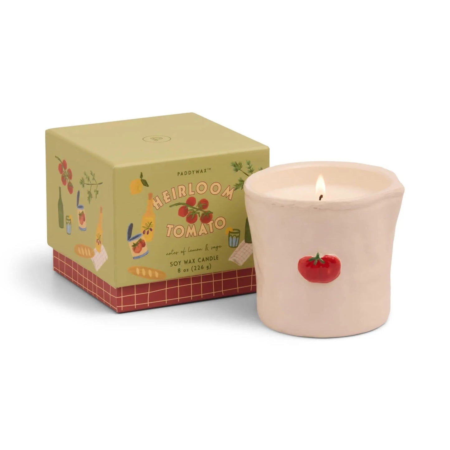 The Bistro Candle - Heirloom Tomato is a lit soy wax candle in a cream container with a hand-painted tomato icon, paired with its decorative Paddywax Bistro box labeled Heirloom Tomato.