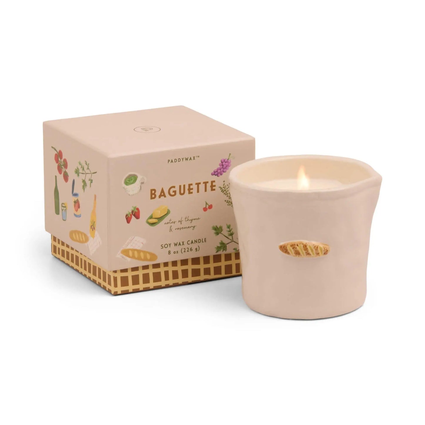 The Bistro Candle - Baguette, a lit soy wax candle in a beige ceramic holder with a baguette motif, sits next to its illustrated box inspired by culinary culture.