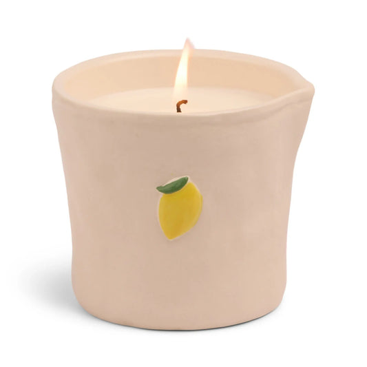The Bistro Candle - Meyer Lemon features a lit white candle in a cream ceramic holder, adorned with a small painted Meyer Lemon, from the Bistro Collection.