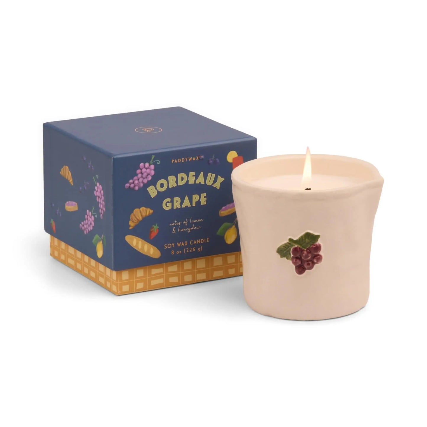 The Bistro Candle - Bordeaux Grape, a soy wax candle in a cream grape-motif container, sits beside its blue box—an aromatic piece inspired by culinary culture.