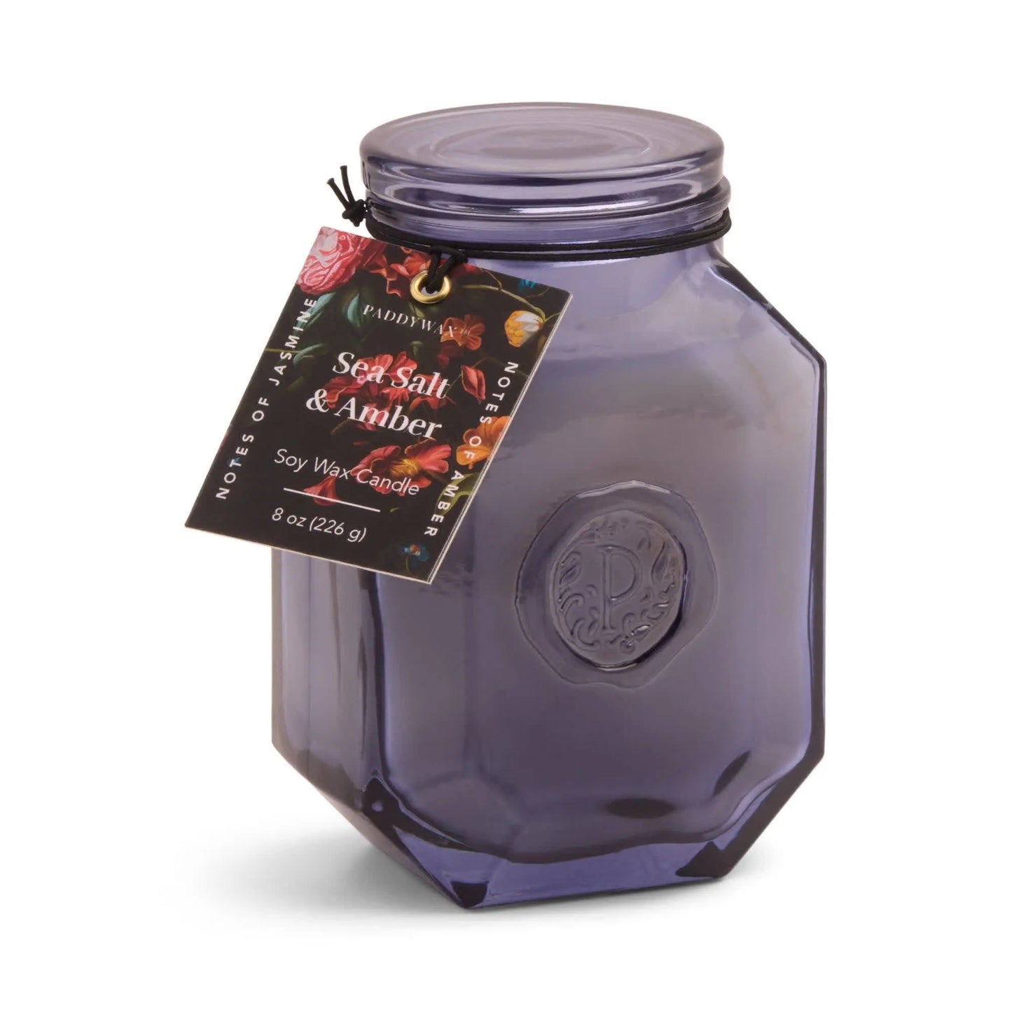 The Botanica Candle - Sea Salt + Amber is an 8 oz (226 g) purple glass jar candle with a black lid, part of the Luxurious Botanica Collection, presented in an elegant vessel and labeled as a soy wax candle.