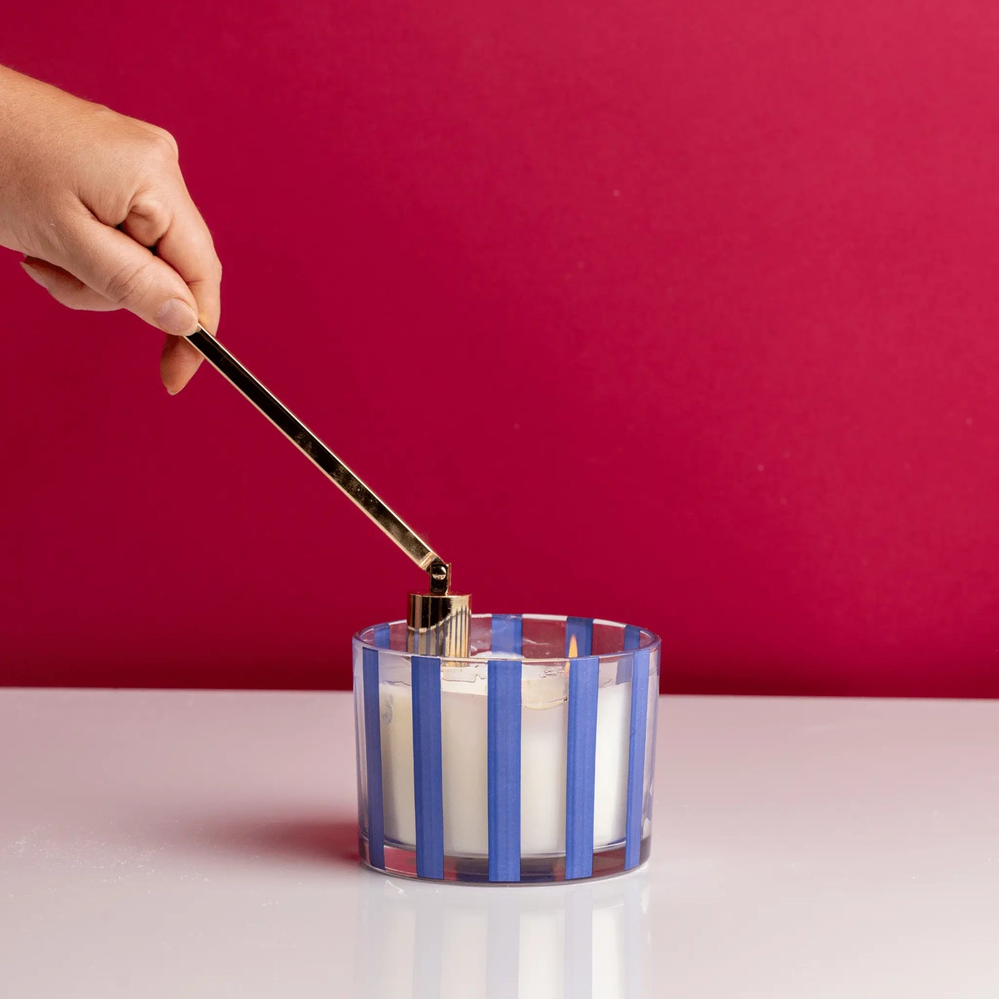 Brass Candle Snuffer snuffing candle on white table with a red background