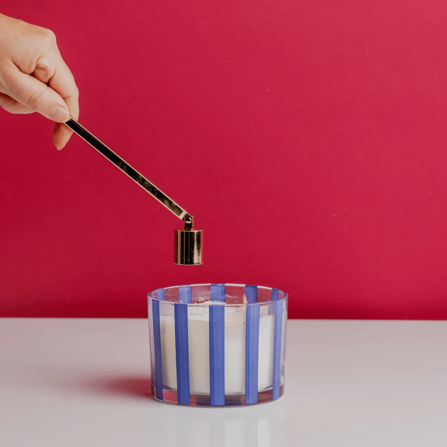 Brass Candle Snuffer hovering above candle on white table with a red background