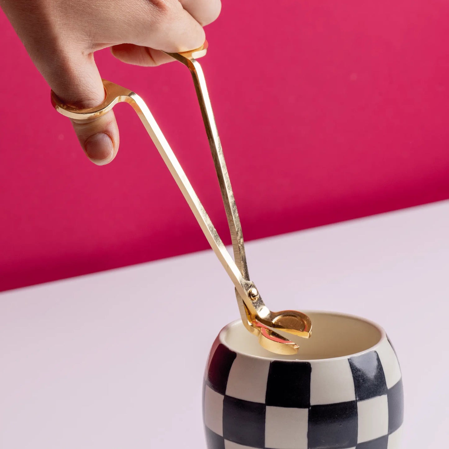 Candle on white table with red background having wick trimmed by Brass Wick Trimmer