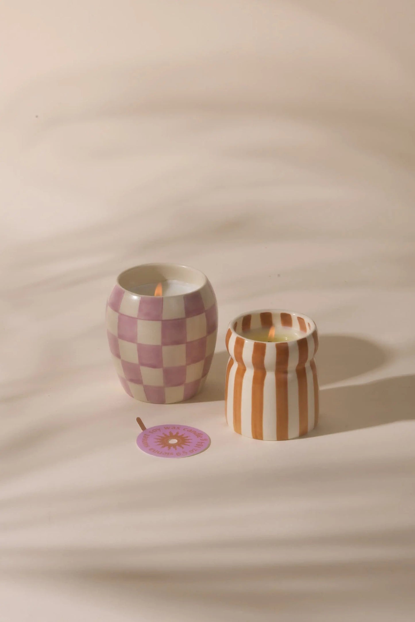 The Cabana Rust Candle - Sienna Sunset features a hand painted candle in a patterned ceramic holder with orange stripes, paired with a purple flower-shaped coaster from the Cabana collection.