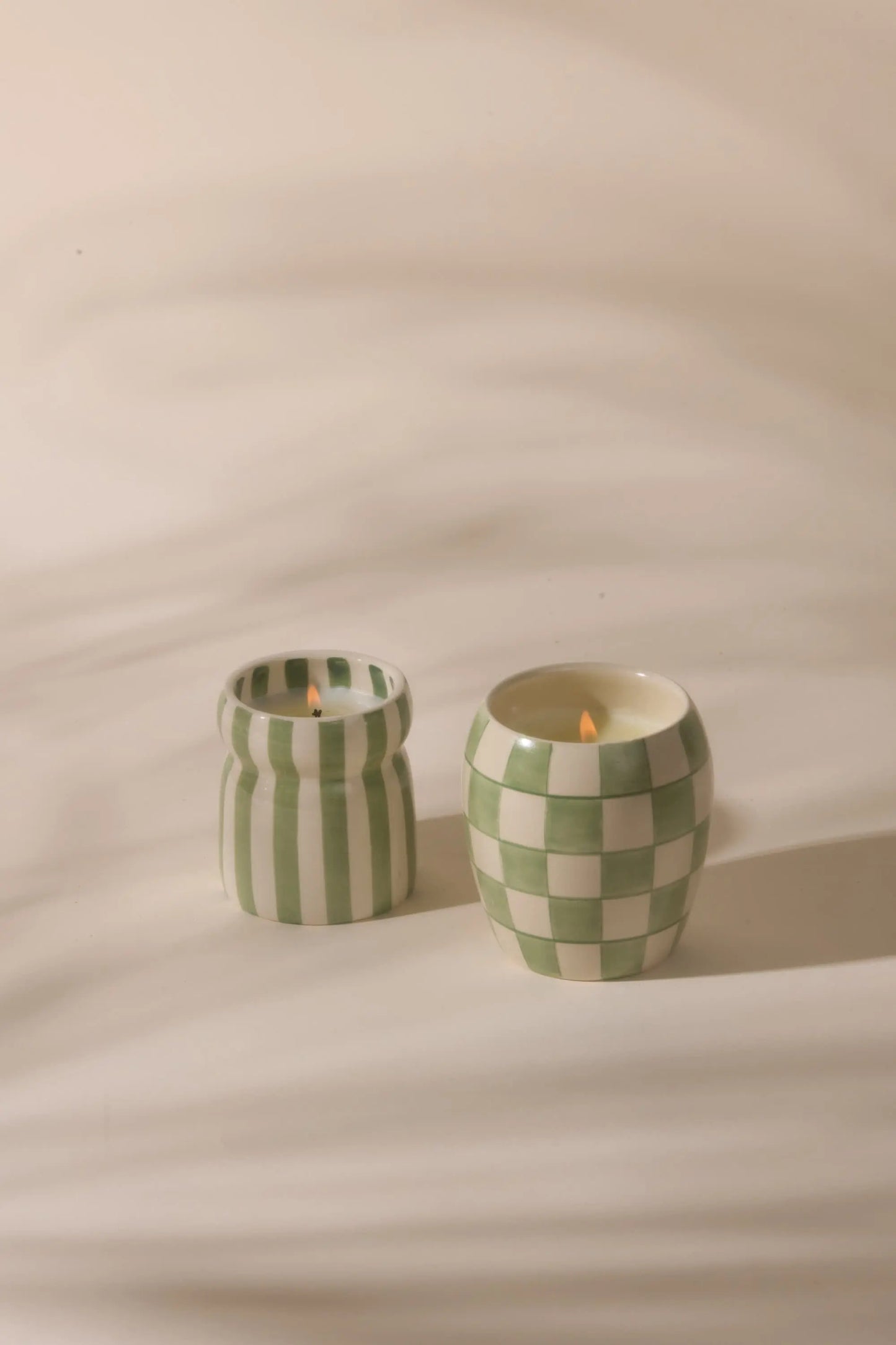 Two lit Cabana Sage Candle - Bora Bora in hand-painted green and white holders, one striped, one checkered, evoke soothing island notes.