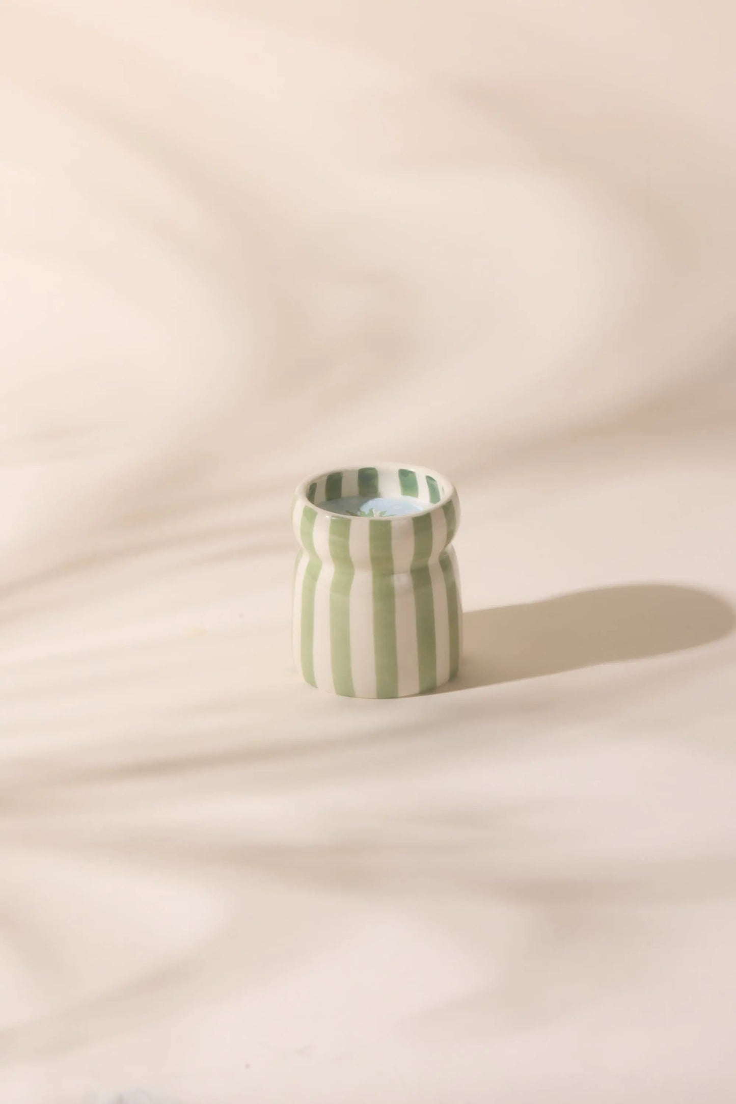 The Cabana Sage Candle - Bora Bora, featuring vertical green and white stripes, sits on a light surface and casts a shadow to the right.