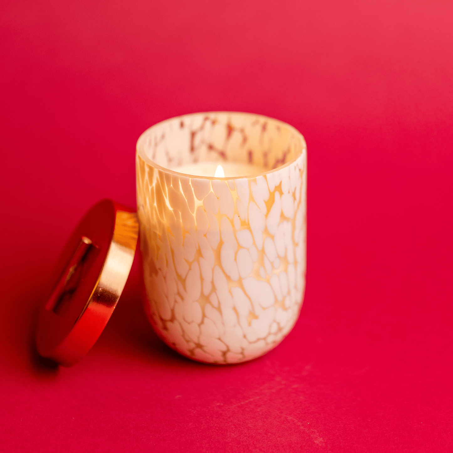 White Blown Glass Candle lit with lid leaning on it on red background