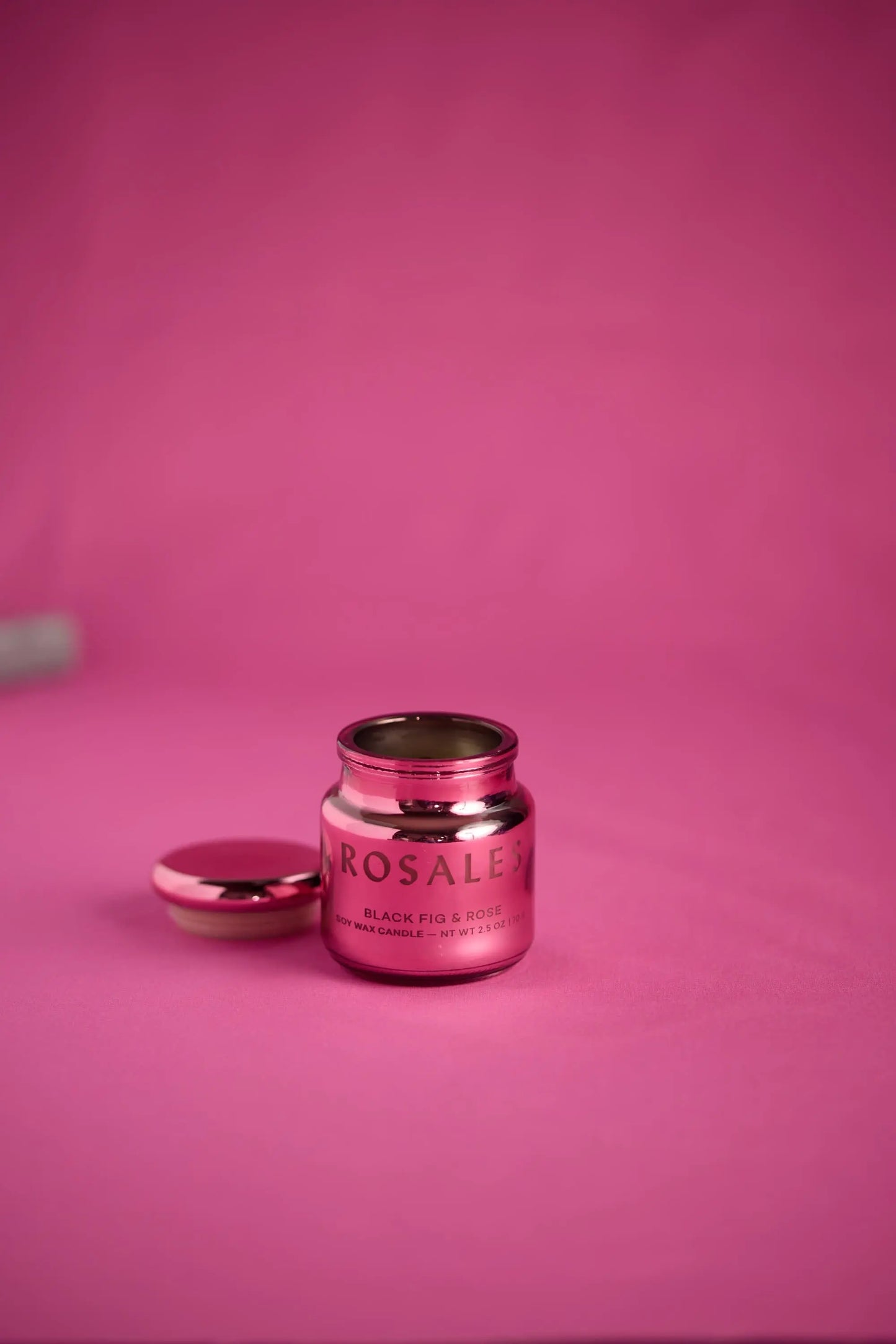 A small, metallic pink Chroma Candle - Saffron Rose, crafted from electroplated glass with its lid off, rests on a pink surface—promising a unique scent experience against a matching background.