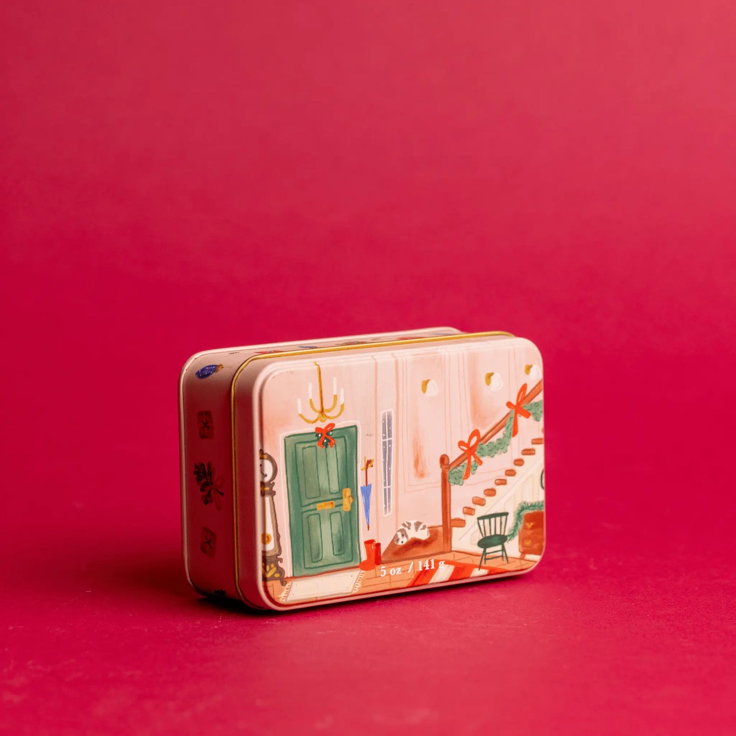 5 oz holiday tin with custom artwork of a room with holiday decor; tin sits on a red background