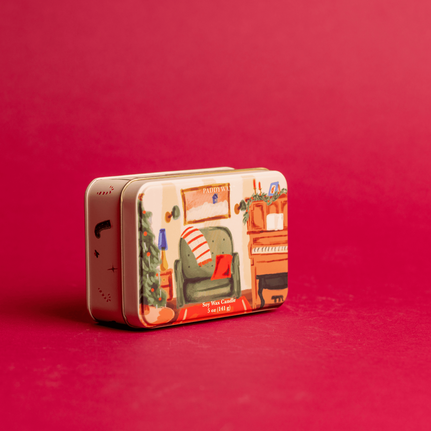 On a red background, 5 oz holiday tin with custom artwork; lid shows family room with piano and decorated tree