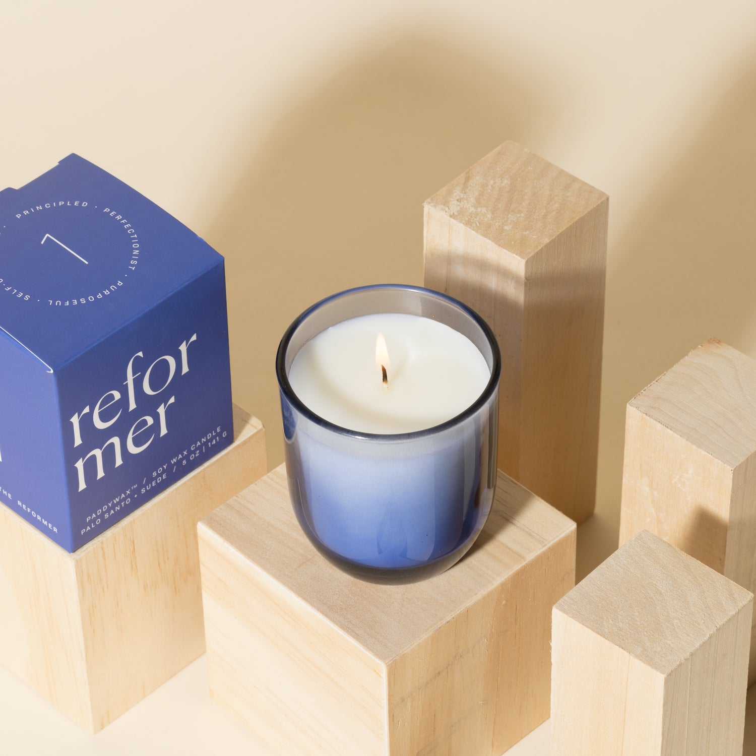 Blue candle with white soy wax burning with blue packaging near candle - Enneagram Candle Paddywax for Enneagram 1 the reformer