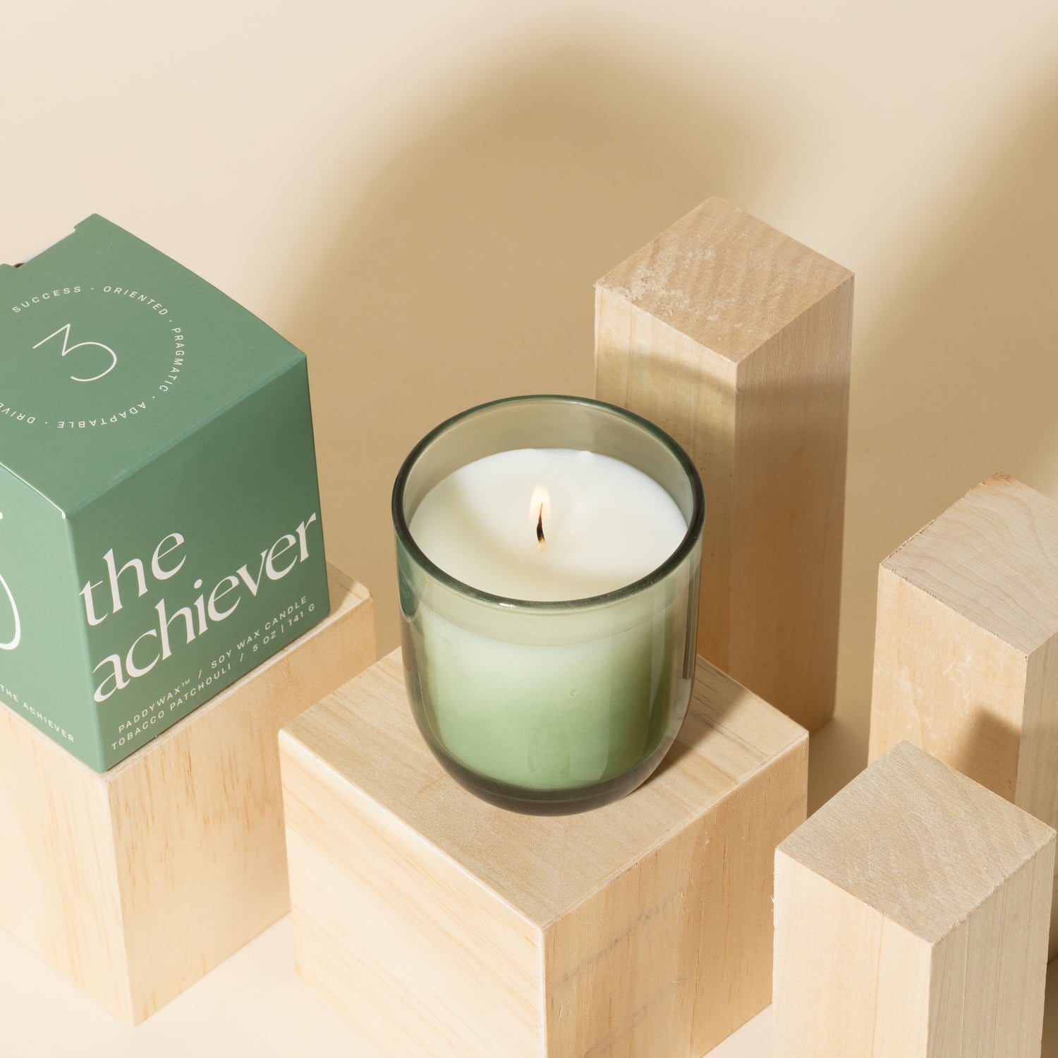 Green candle with white soy wax burning with green packaging near candle - Enneagram Candle Paddywax for Enneagram 3 the achiever