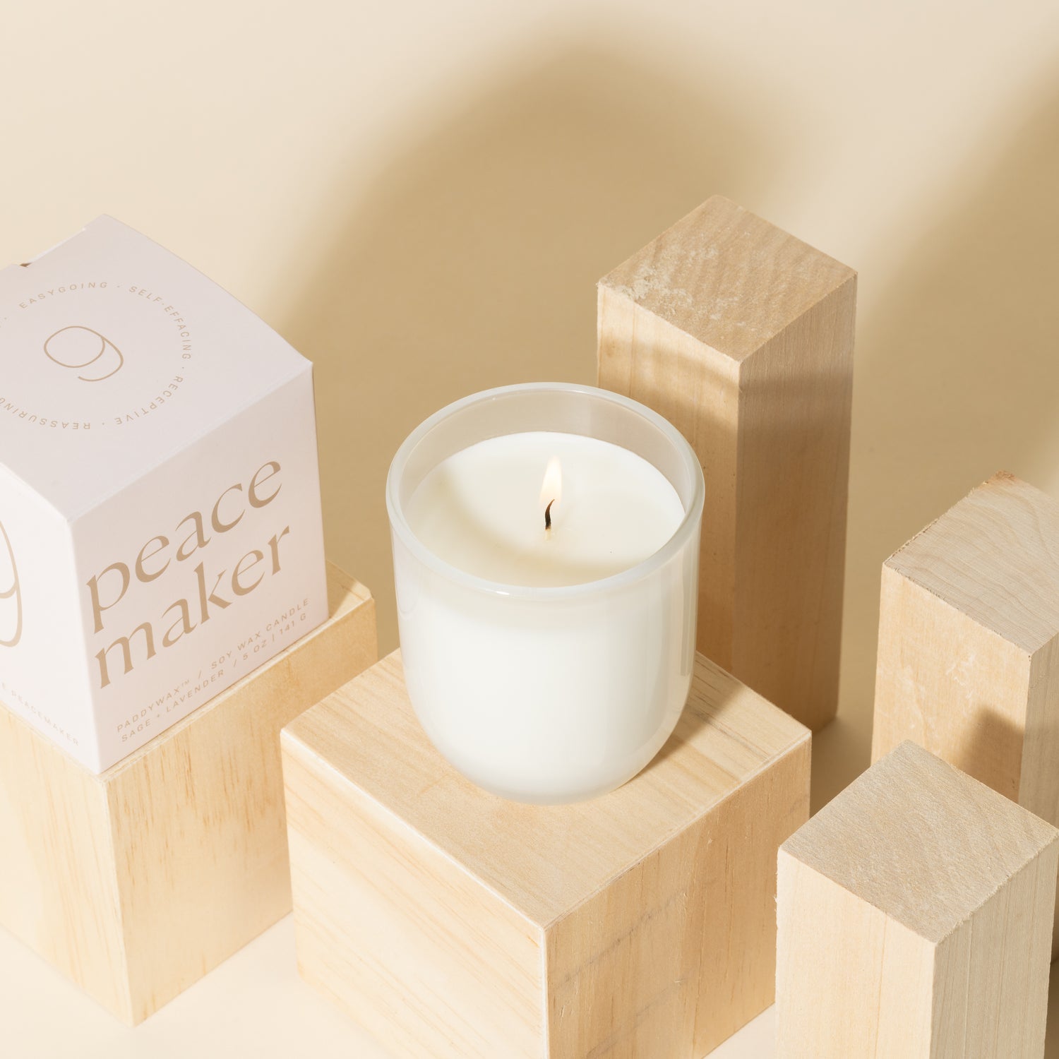 White candle with white soy wax burning with white packaging near candle - Enneagram Candle Paddywax for Enneagram 9 the peacemaker