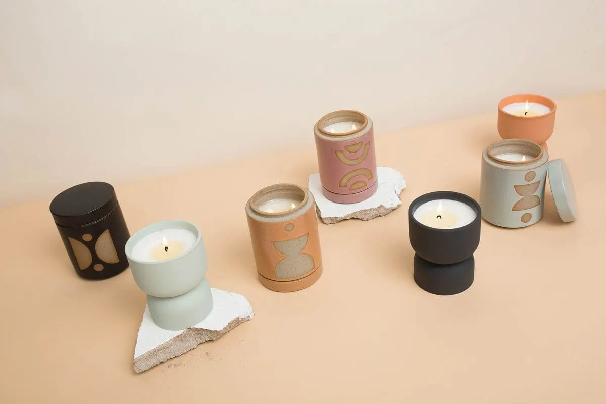 Six Palo Santo Suede - Form 6 oz decorative ceramic candles in minimalist, desert-inspired containers are displayed on a beige surface with white stone accents. Each vessel can be reused as a planter after the candle is finished.
