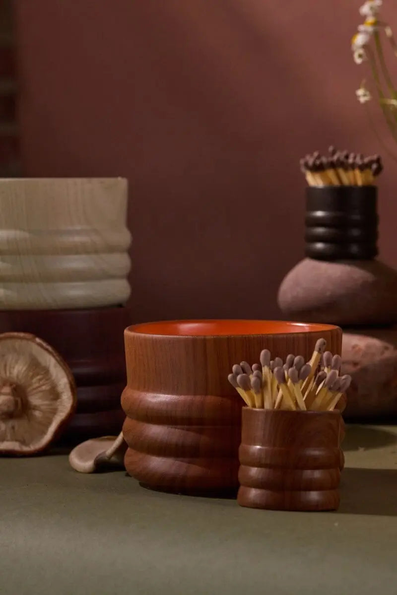 Wooden cups and containers holding matches are displayed on a green surface with a dried mushroom and vase, evoking the earthy ambiance of Grain Candle - Redwood & Amber and the scent of a redwood forest.
