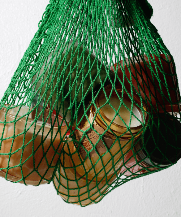 Glass jars with gold lids are held inside a green mesh bag against a plain white background.