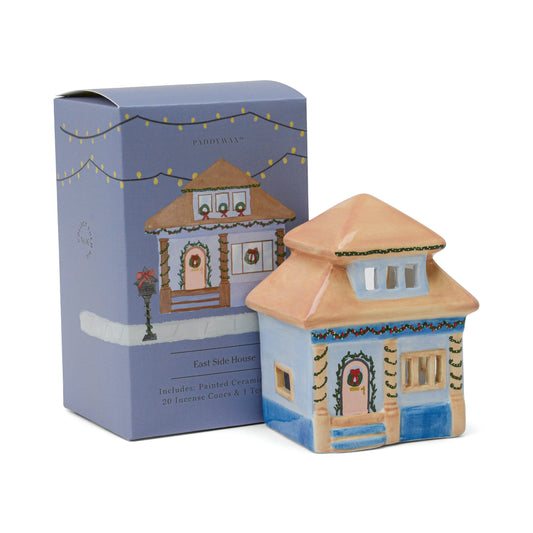 The East Side House, Number 06 of a Collectible Series, is a painted ceramic house Tea Light Holder displayed before a box featuring an illustration of the same festive holiday-decorated home.