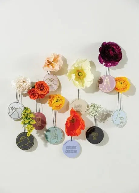 The Impressions Car Fragrance - Violet Vanilla Thankful For You features colorful flowers and round badges with hand gesture illustrations and short phrases, all set against a light background for a fresh look.