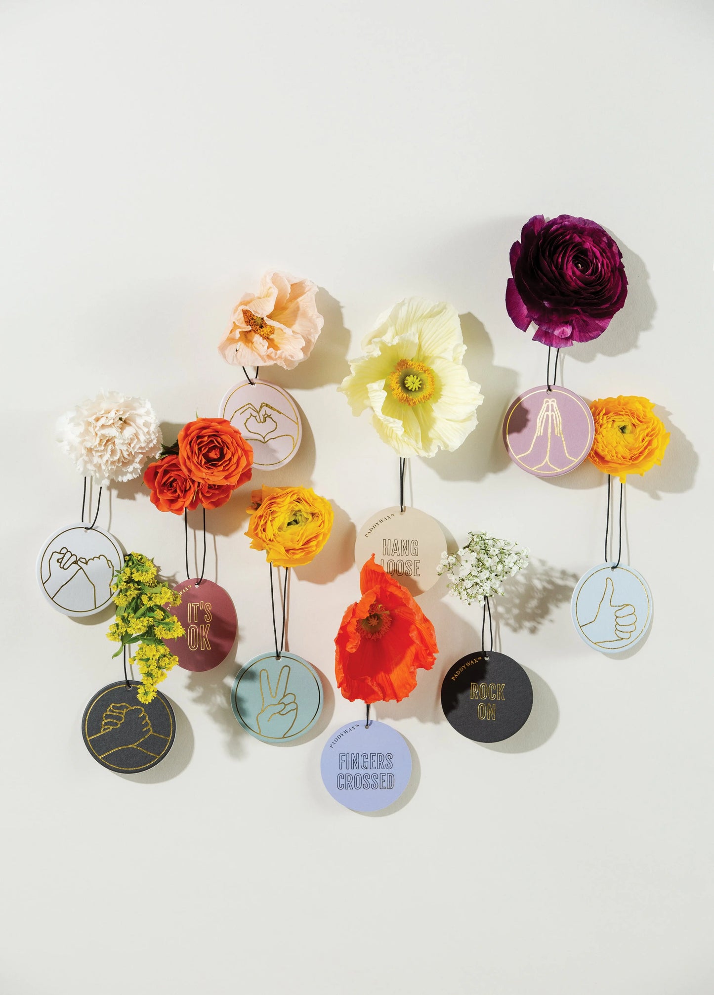 Colorful flowers are attached to circular tags featuring hand gesture illustrations and the phrase Rock On, showcasing the Impressions Car Fragrance - Leather + Oakmoss against a light background.