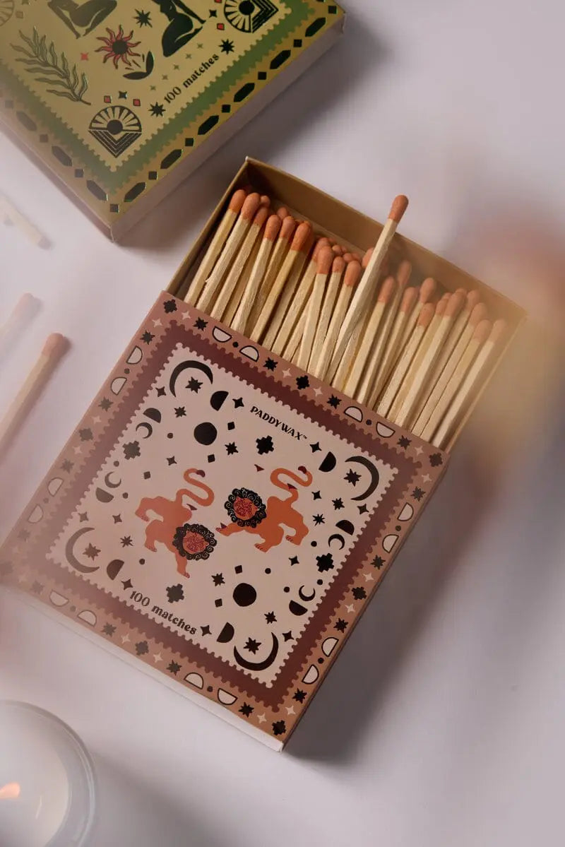 The Jumbo Boxed Matches - Lions features an open matchbox adorned with two lions, floral and geometric designs, containing several jumbo matches inside and a few loose ones nearby.