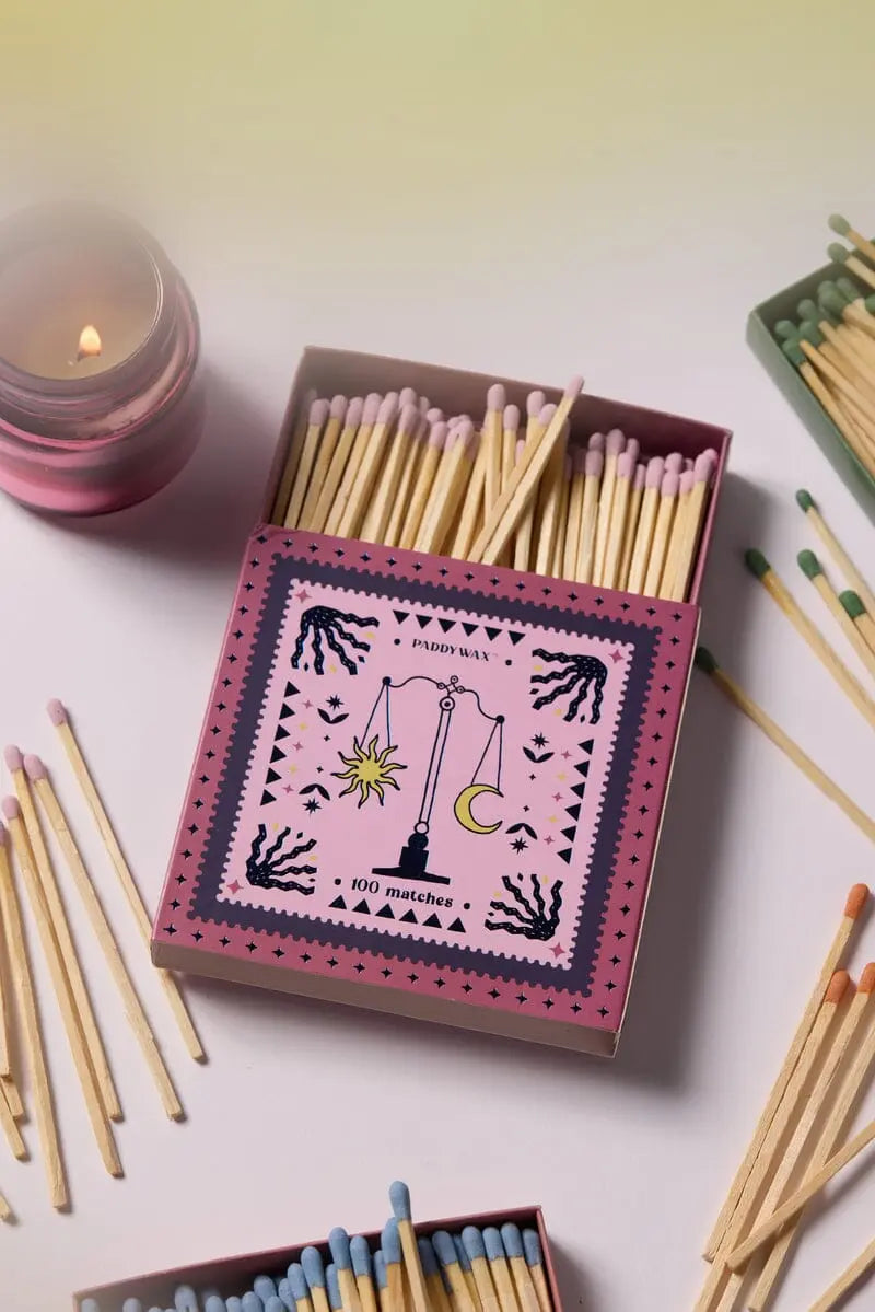 The Jumbo Boxed Matches - Balance features a pink matchbox with a scale illustration, surrounded by scattered matches and a lit pink candle.