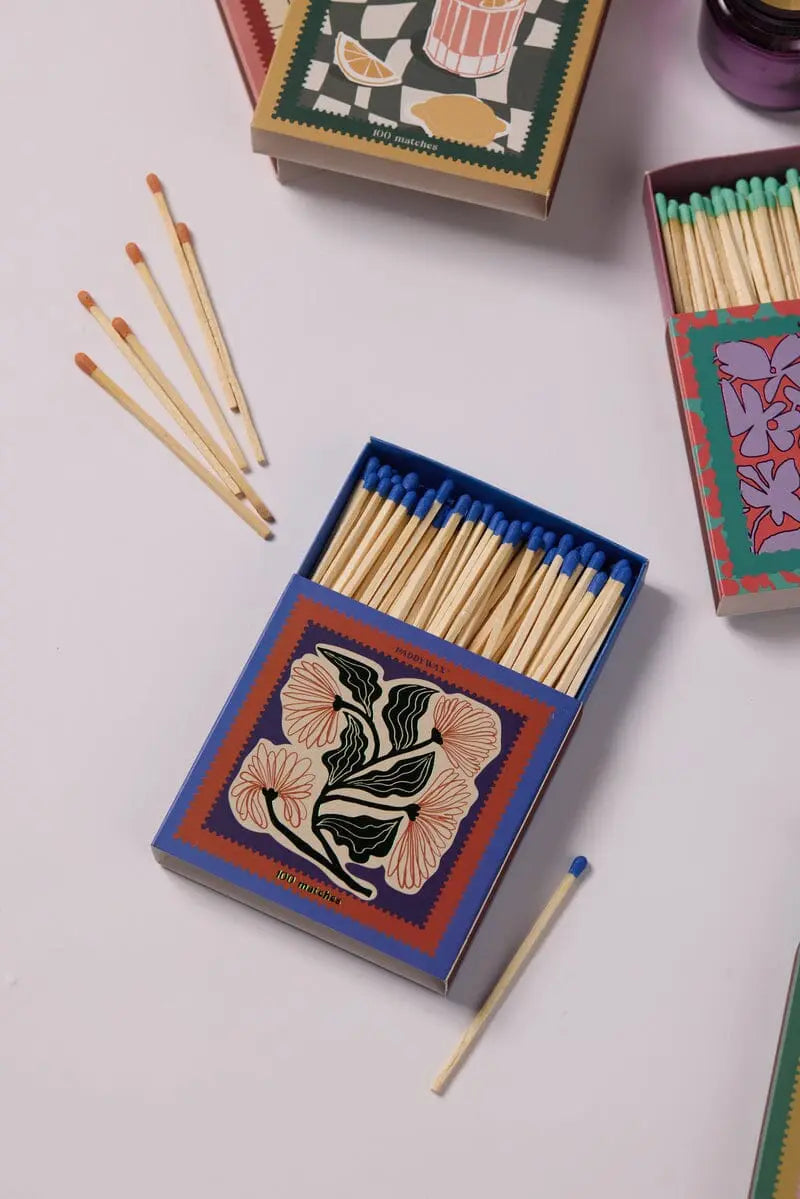 The Jumbo Boxed Matches - Floral are displayed with open boxes revealing jumbo matches with colorful tips, some scattered on a white surface—perfect for lighting your favorite Paddywax candle.