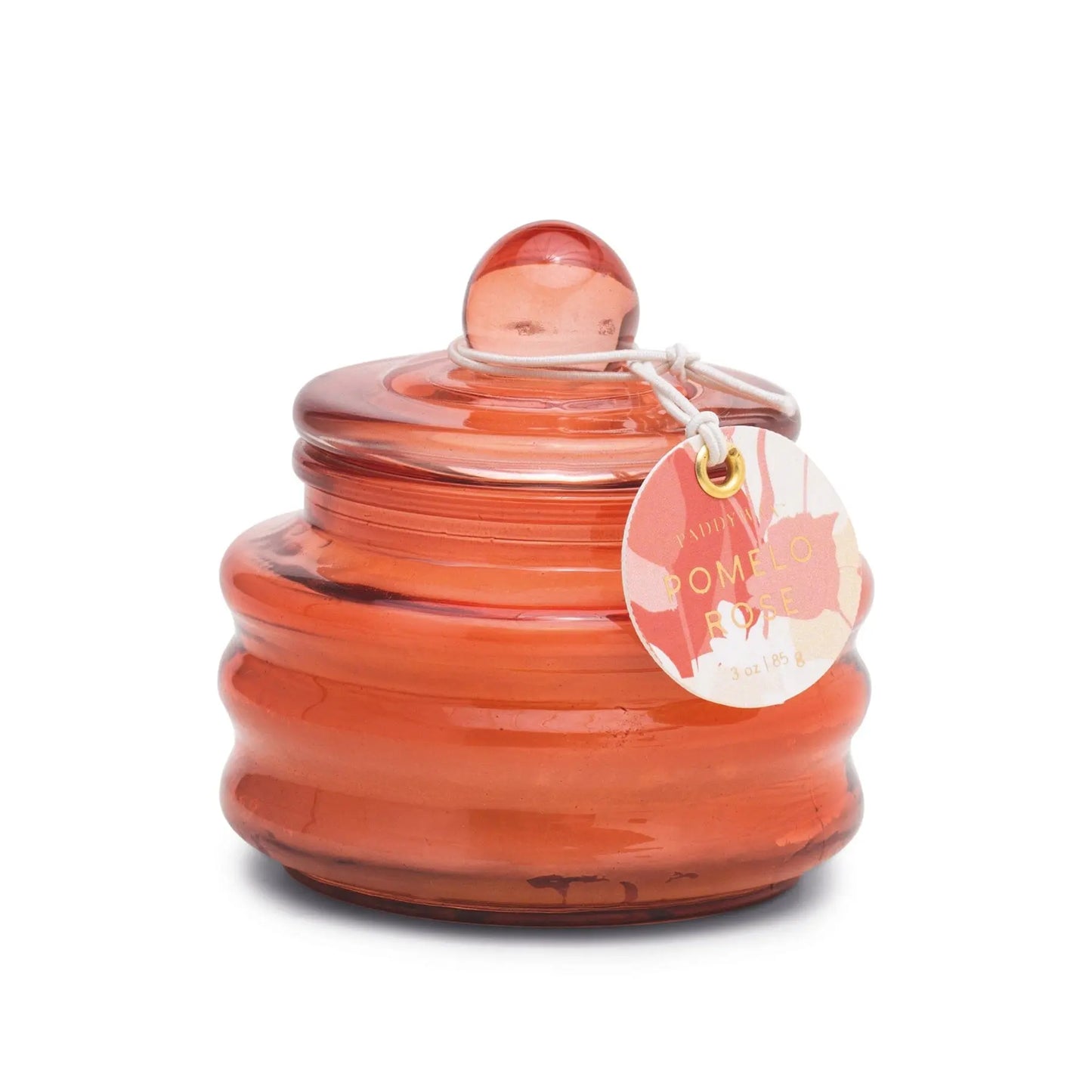 The Beam 3oz Glass Candle - Pomelo Rose is a small orange candle jar with lid and round handle, decorated with a white string and tag—ideal for adding ambient light to any space.