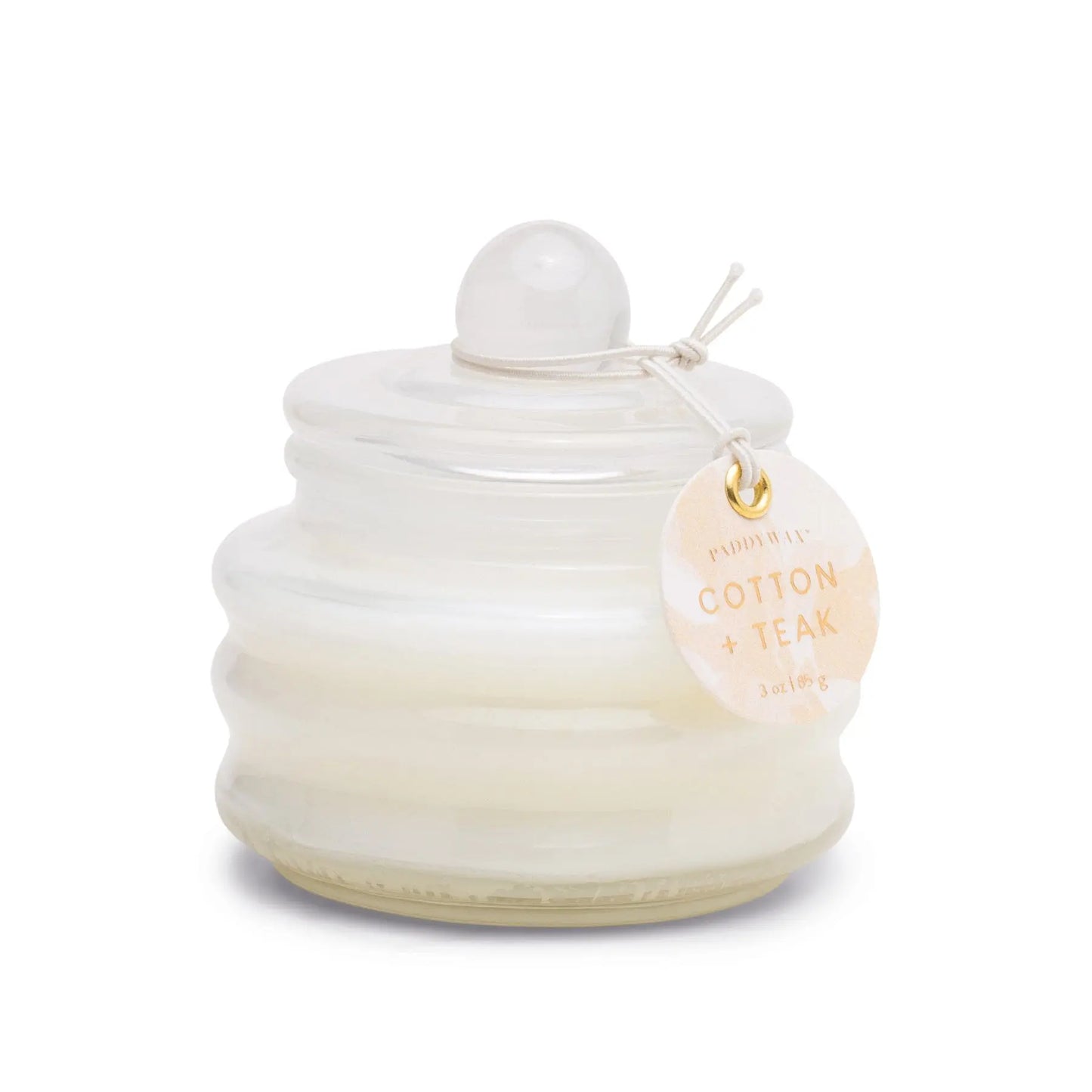 The Beam 3oz Glass Candle - Cotton & Teak features a small white candle in a round, ribbed glass jar with a lid and tag, perfect for adding ambient light and luxurious scent to any space.