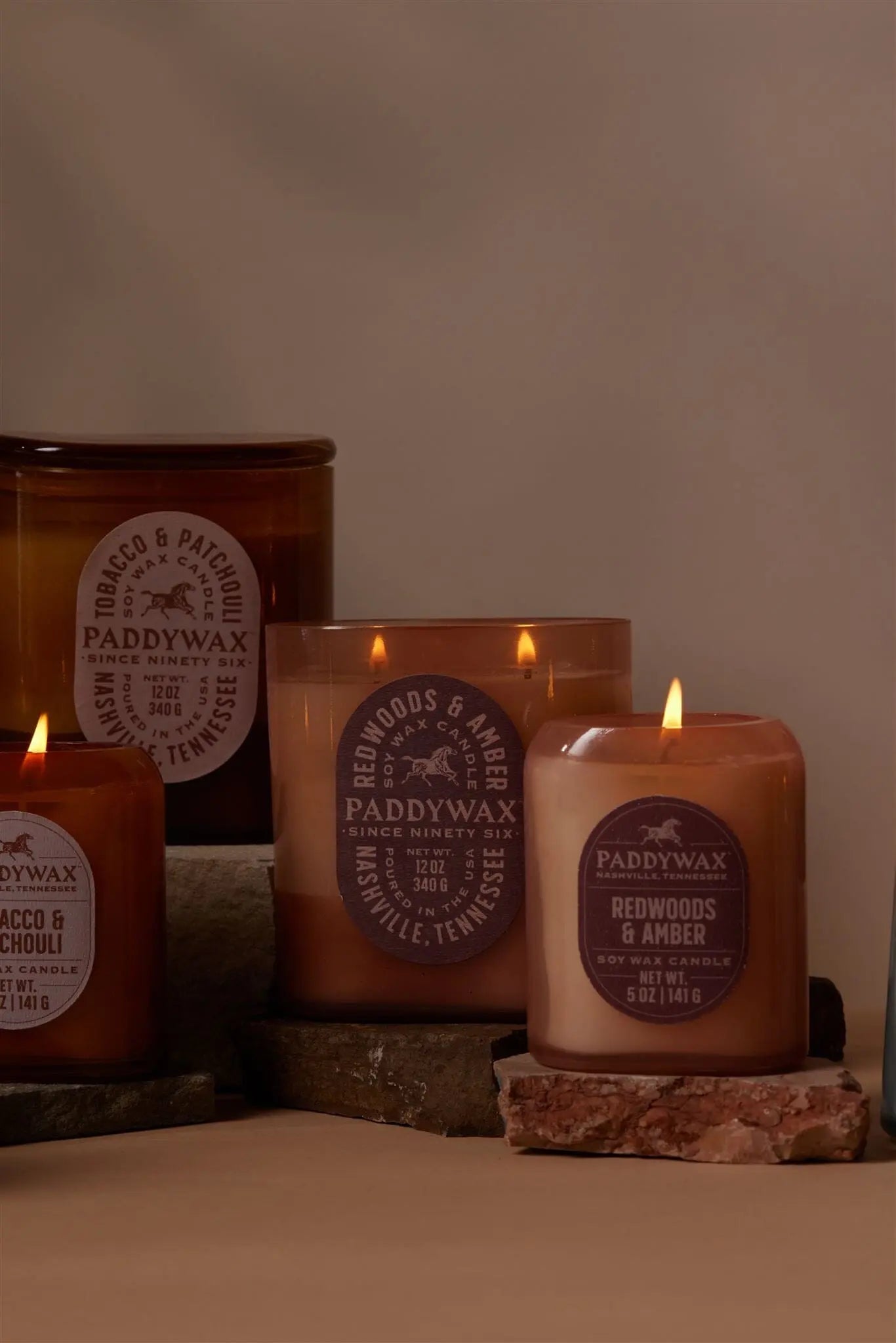 The Vista 5 oz Candle in Redwoods & Amber by Paddywax, styled in brown and beige, sits on stone slabs—an ideal modern decor piece with a luxurious fragrance.