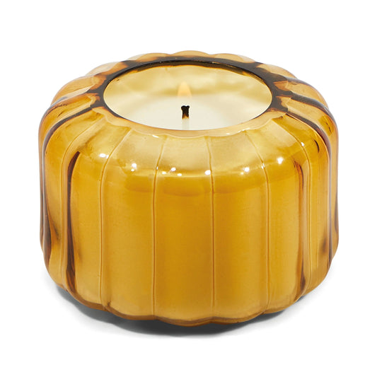The Ripple Candle- Golden Ember glows with a lit wick in a round, ribbed amber glass container, bringing a vintage charm.