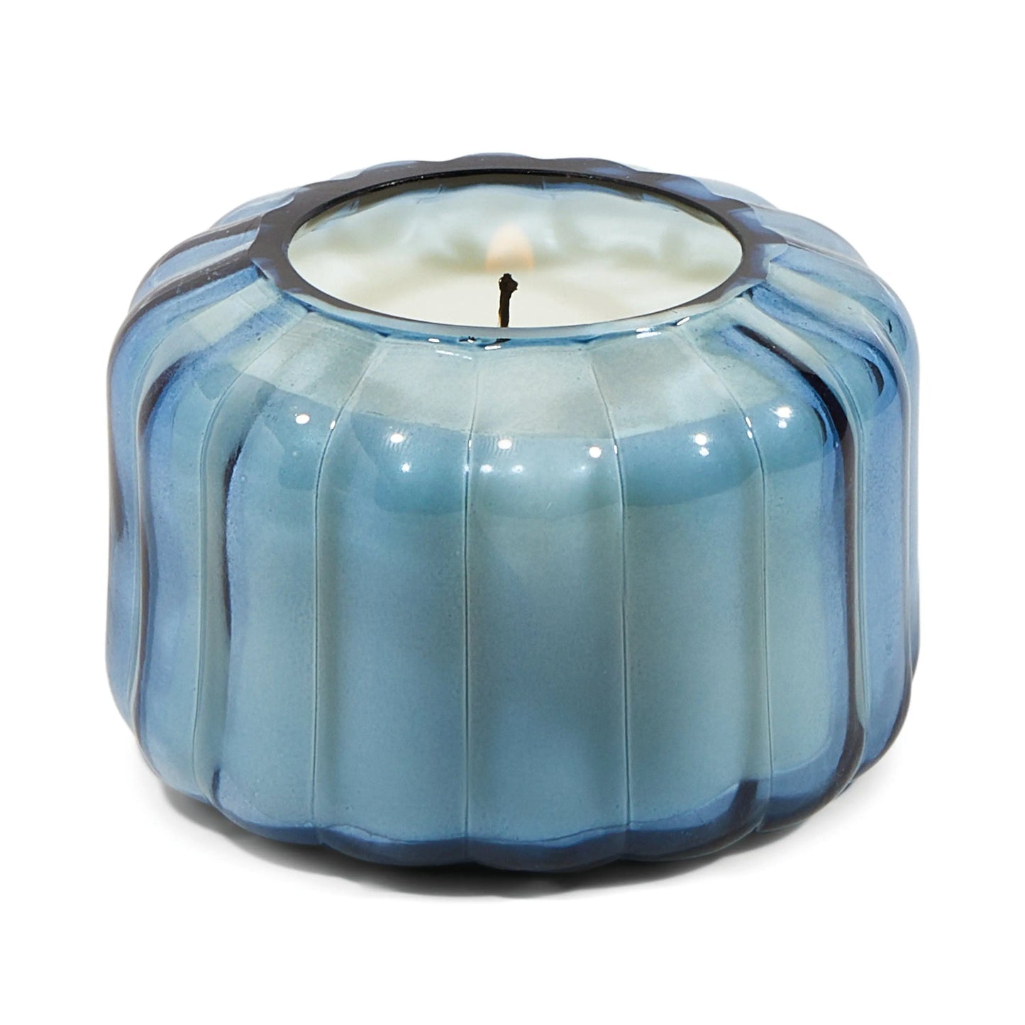 The Ripple Candle - Peppered Indigo features a blue, round glass holder with vertical grooves and a white candle inside, adding vintage flair to your colored glass collection.