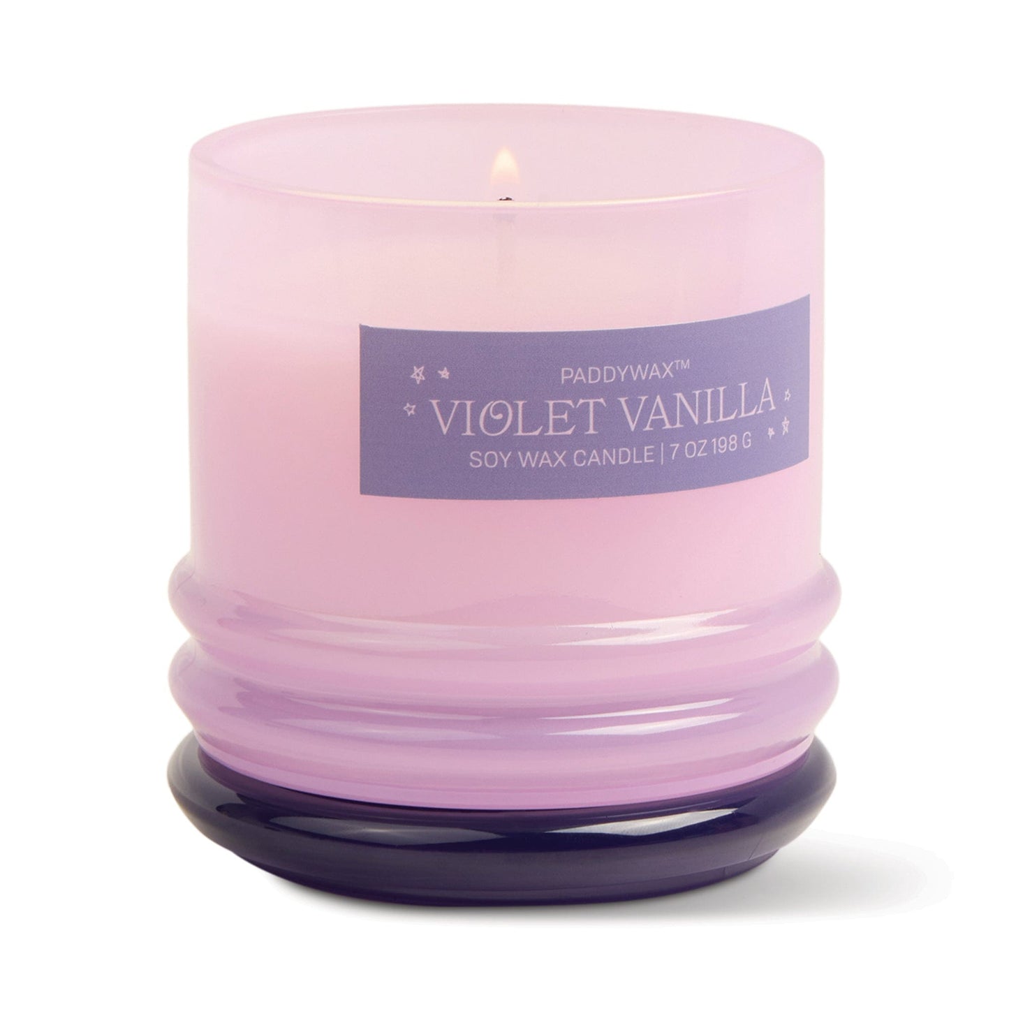 A lit Violet Vanilla - Stack 7 oz Candle in a reusable glass vessel features a soft purple hue and an elegant rounded base, with a soothing floral scent and label reading Paddywax Violet Vanilla Soy Wax Candle 7 oz 198 g.