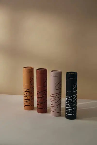 Four boxes of Burnt Orange & Peach Tube Tapers—set of 4—stand upright on a light surface, adding stylish, colorful candles to any sophisticated dining setup with a sleek, modern touch.