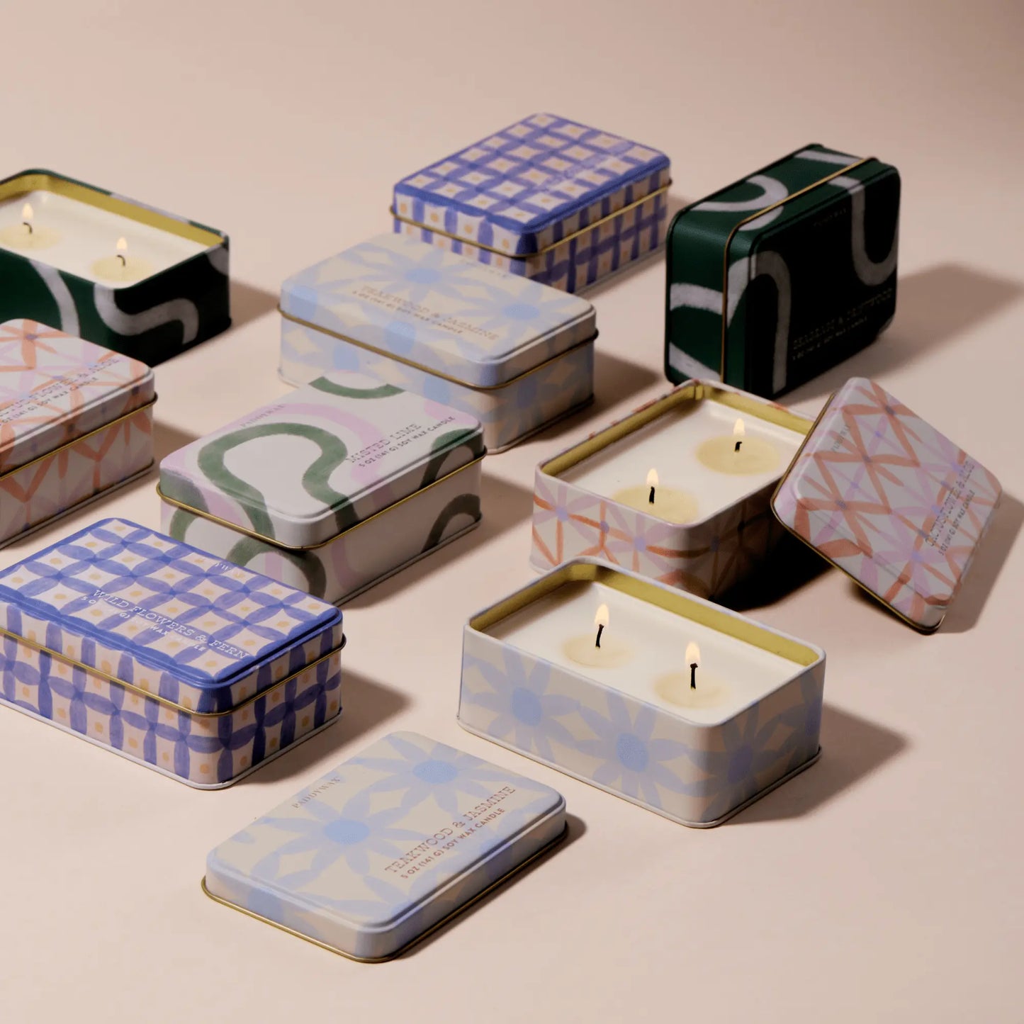 Everyday Tins 5 oz. Candle in Cactus Flower & Aloe scent are shown on a neutral surface in assorted patterned tins, some with lids off to reveal single or double wicks.