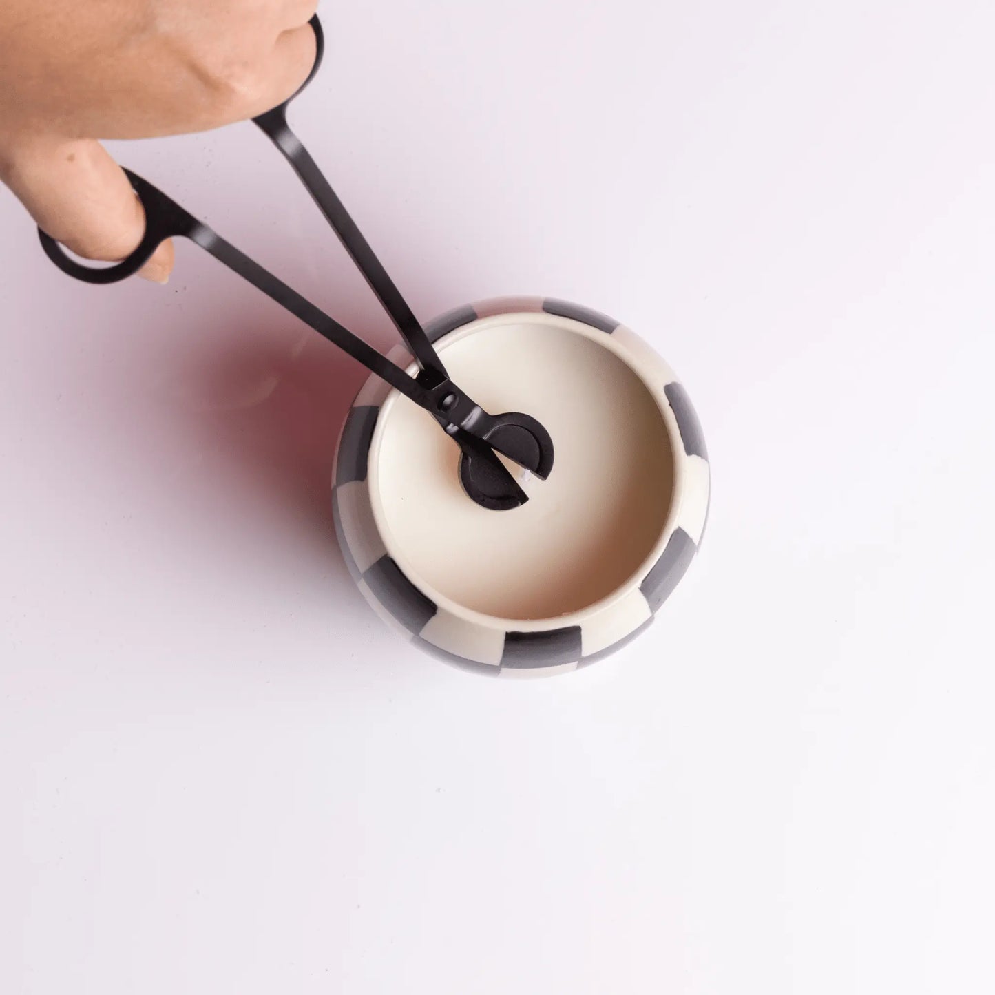 Human hand trimming wick with Black Matte Wick Trimmer on white background