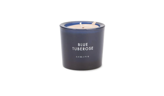 A Botany - Blue Tuberose 2.5 oz votive glass candle with white text from the Botany Collection is displayed on a plain white background.